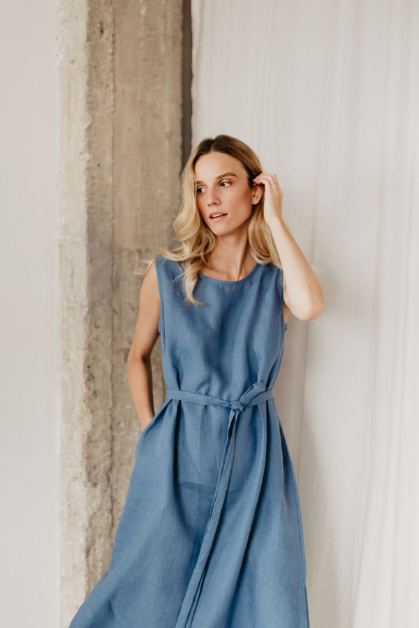 Mėlyna lininė suknelė su dirželiu švelniai pabrėžia figūrą ir suteikia elegancijos.