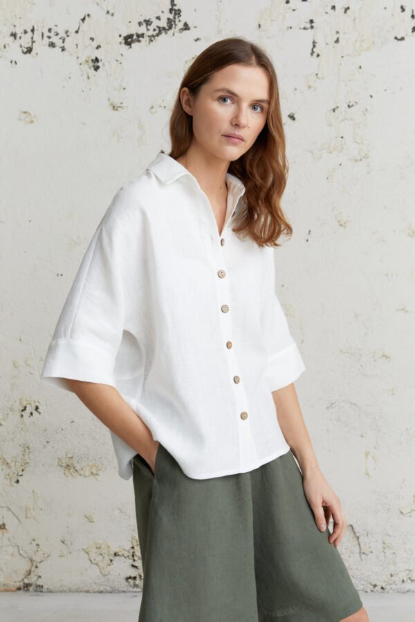 Balti lininiai marškiniai su trijų ketvirčių ilgio plačiomis rankovėmis, oversize siluetas ir natūralus audinys.