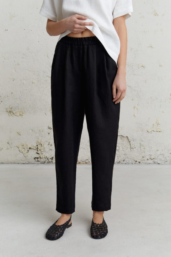 Adatytė siaurėjančios lininės kelnės moterims, juodos, su klostėmis ir kišenėmis, minimalistinis dizainas.