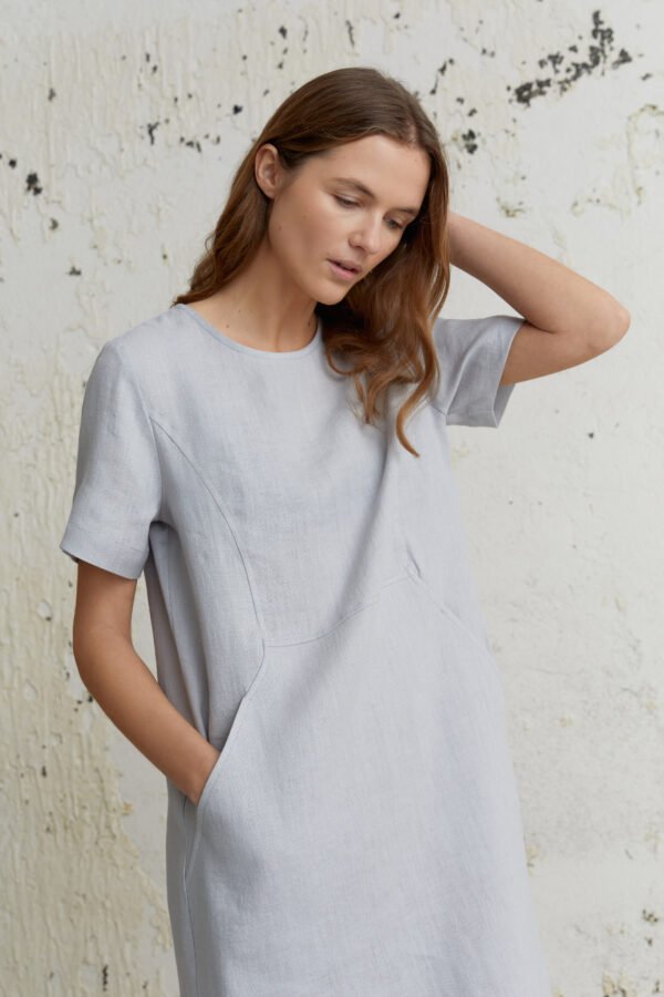 Šviesiai pilkos suknelės detalė – trumpa rankovė, kišenė ir švelni lino tekstūra.